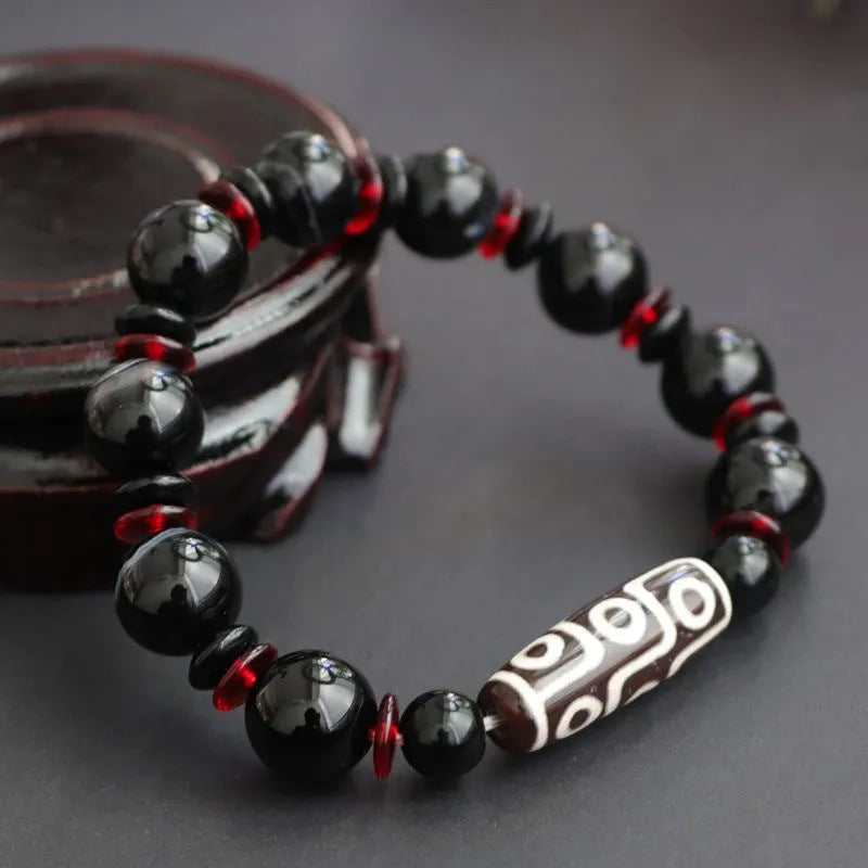 Hand-woven black agate dzi bead bracelet with geometric chalcedony beads on a wrist.