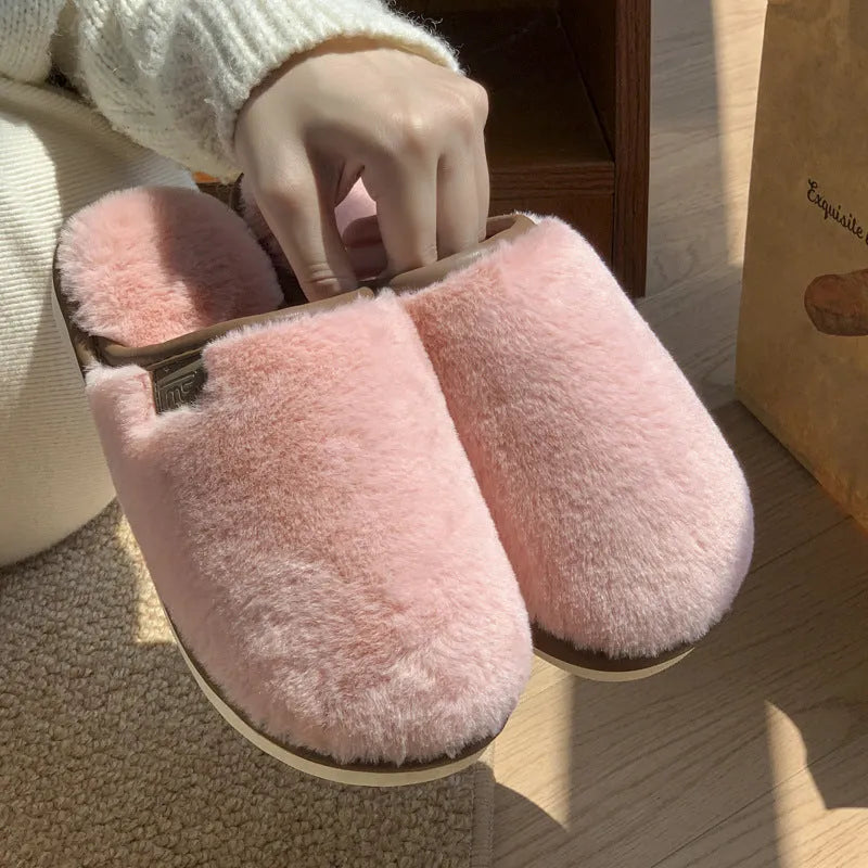 A pair of solid blue plush slip-on house slippers with a non-slip PVC sole and decorative car stitching on the upper.