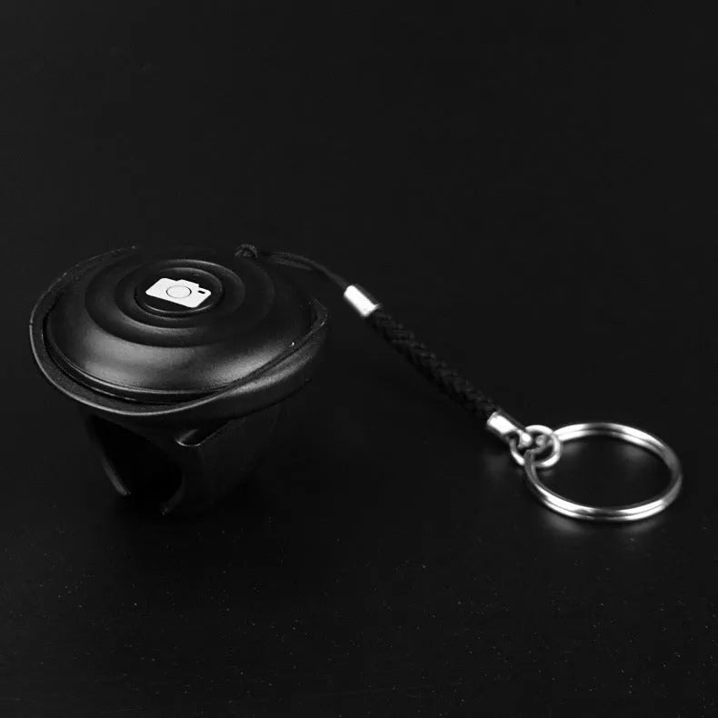 Black Bluetooth remote control for selfies with a single snap button on a white background.