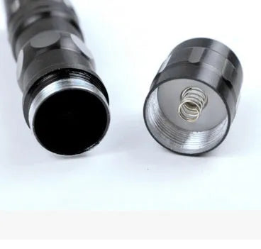 Black aluminium mini LED flashlight showing scale next to a AA battery.