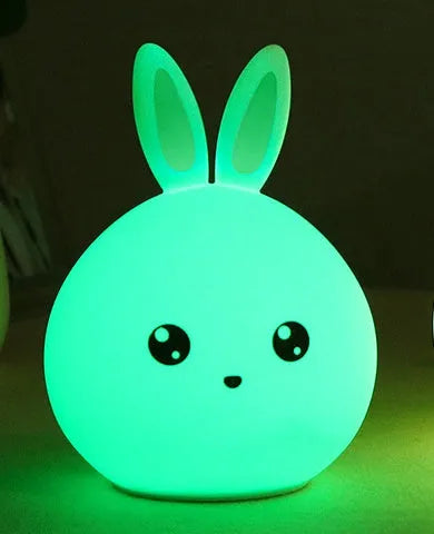 Cute rabbit-shaped night light made of soft silicone with touch sensor, showing seven LED colour options, on a bedside table.