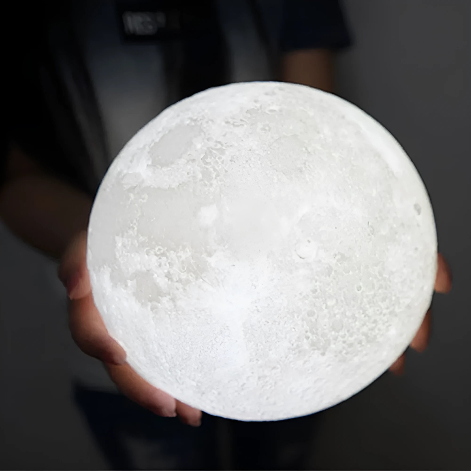 3D printed white moon lamp on a wooden holder, showing detailed lunar surface and a glowing yellow light.