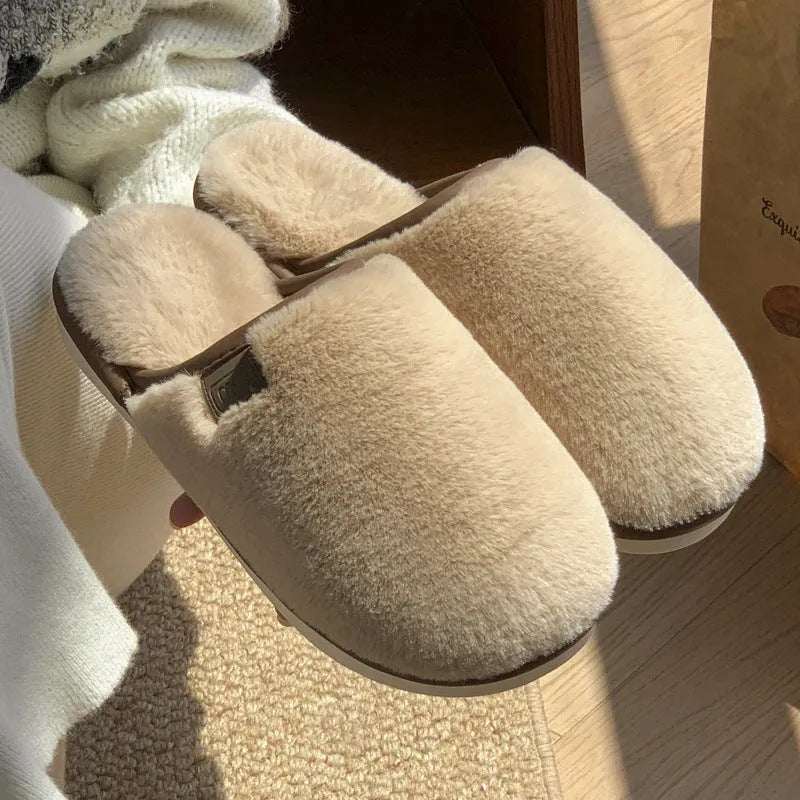 A pair of solid blue plush slip-on house slippers with a non-slip PVC sole and decorative car stitching on the upper.