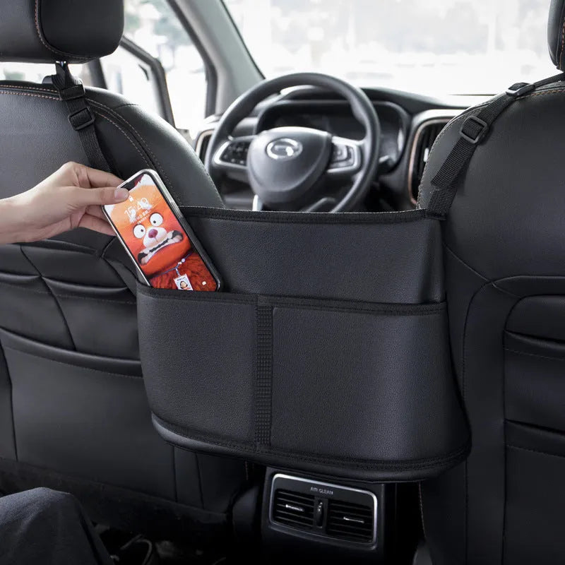 Black leather car seat organiser bag with carbon fibre pattern, shown in a car's centre seat gap.