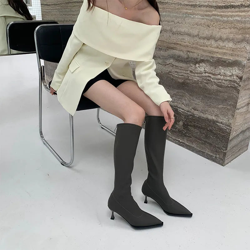 Women's black pointed toe knee-high boots with a stiletto heel and a back zip, shown on a foot.