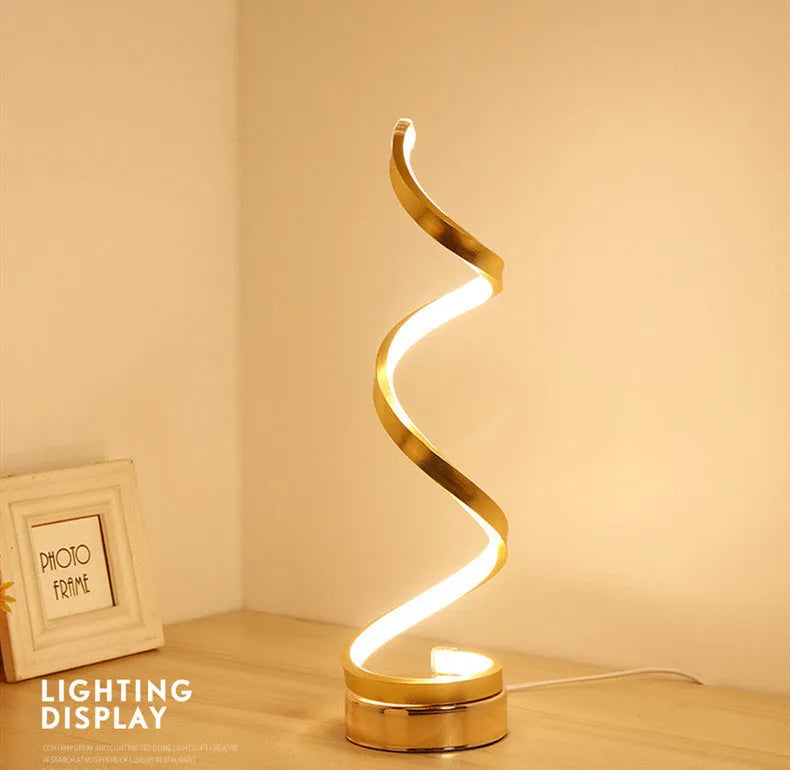 Modern LED table lamp with gold metal base and curved acrylic shade on a desk