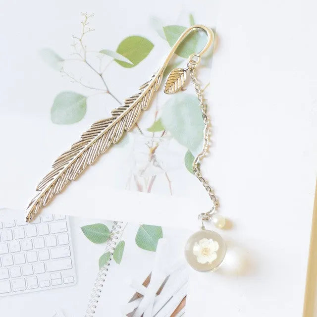 Flat metal bookmark with dried flower inside, showing 12cm length, on an open book.