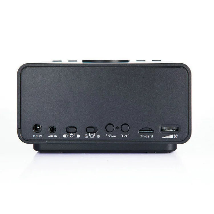Black and white wireless alarm clock speaker with digital display, twin speakers, and a remote control on a wooden surface.