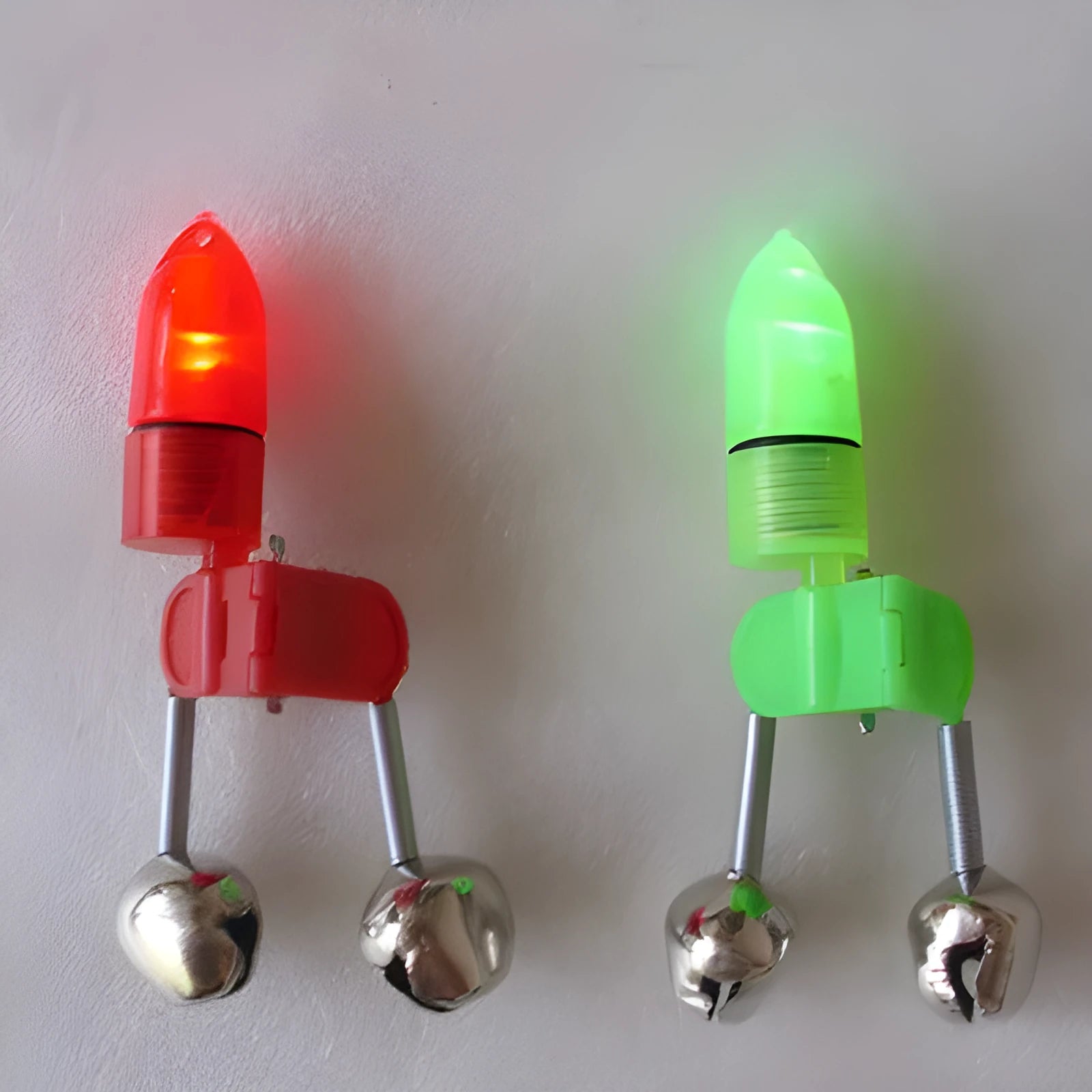 Two fishing bell bite alarms with LED lights, one green one red, clipped onto a fishing rod tip