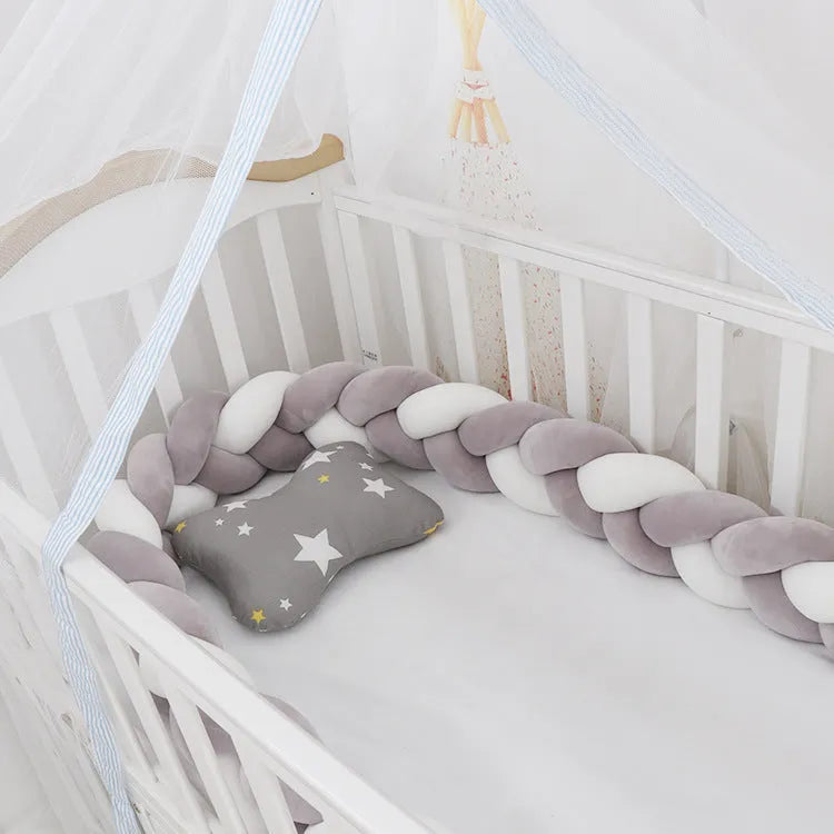 Close-up of a grey braid knot pillow cushion cot bumper fitted around white crib rails.
