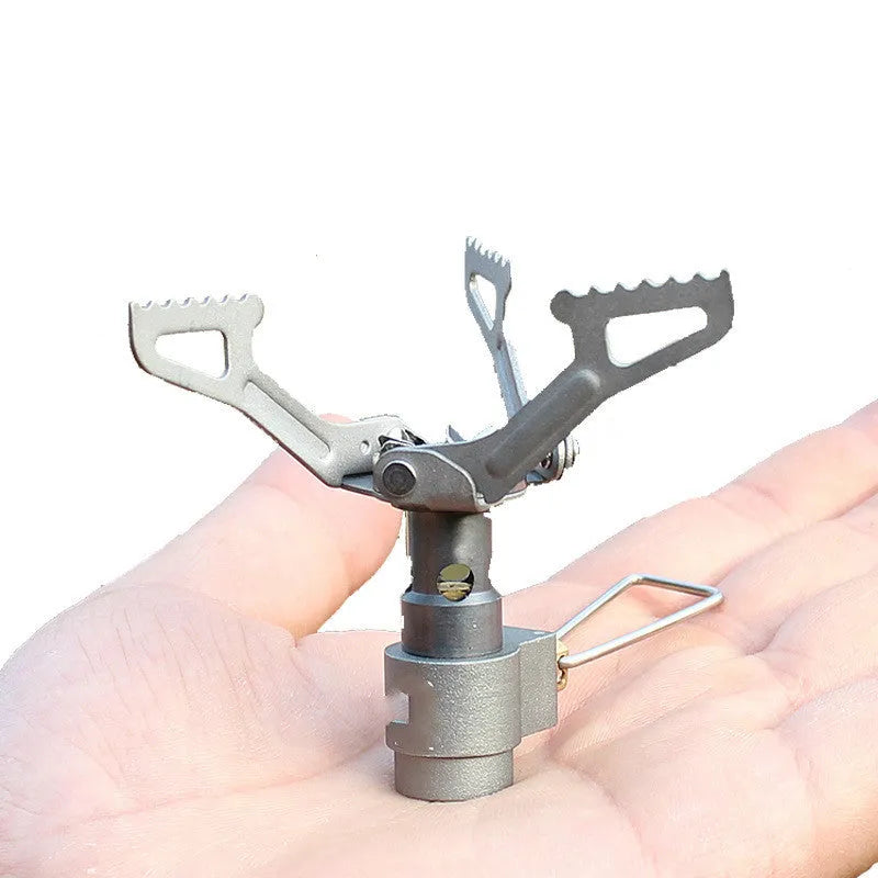 Compact one-piece propane camping stove on rocky ground, fuel canister attached, with a pot boiling.