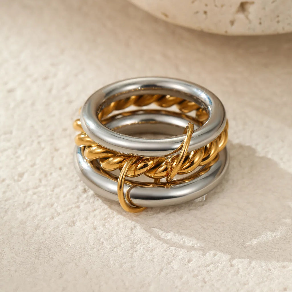 Stacked gold plated stainless steel rings with an exaggerated design on a person's hand.