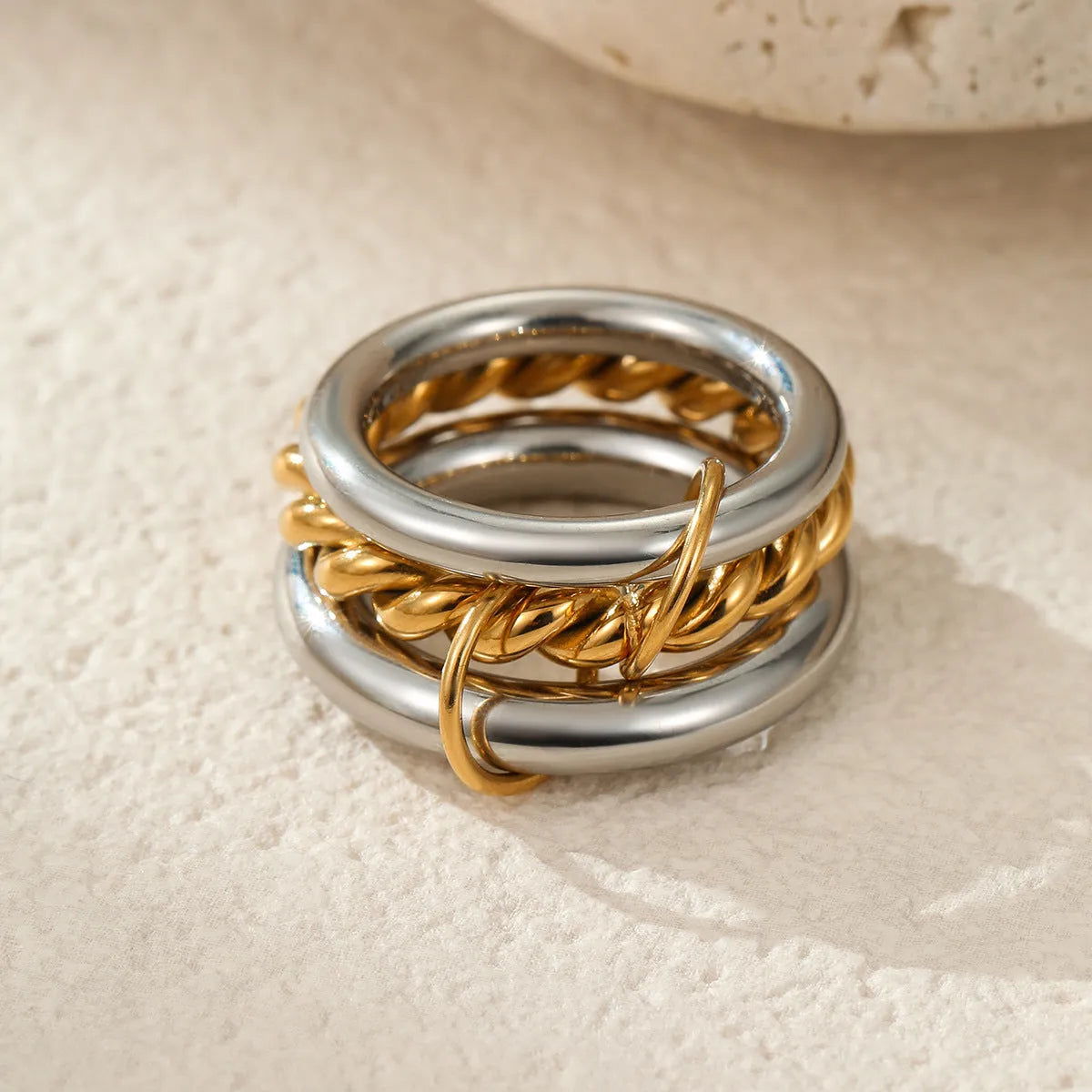 Stacked gold plated stainless steel rings with an exaggerated design on a person's hand.