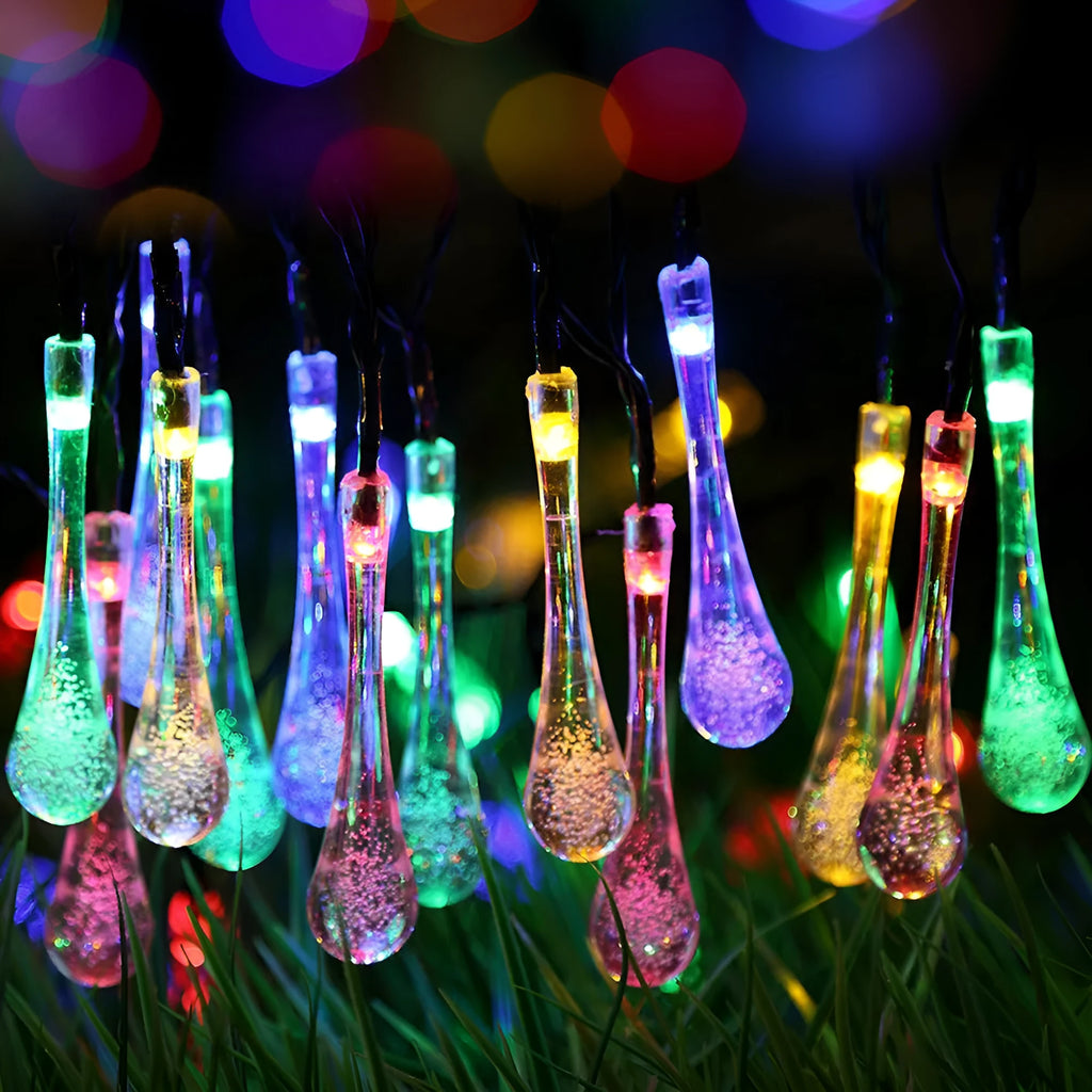 Solar-powered waterproof LED string lights with bubble drop pendants illuminating an outdoor garden space at dusk.