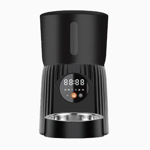 Black automatic pet feeder with digital timer display and remote control on a table.