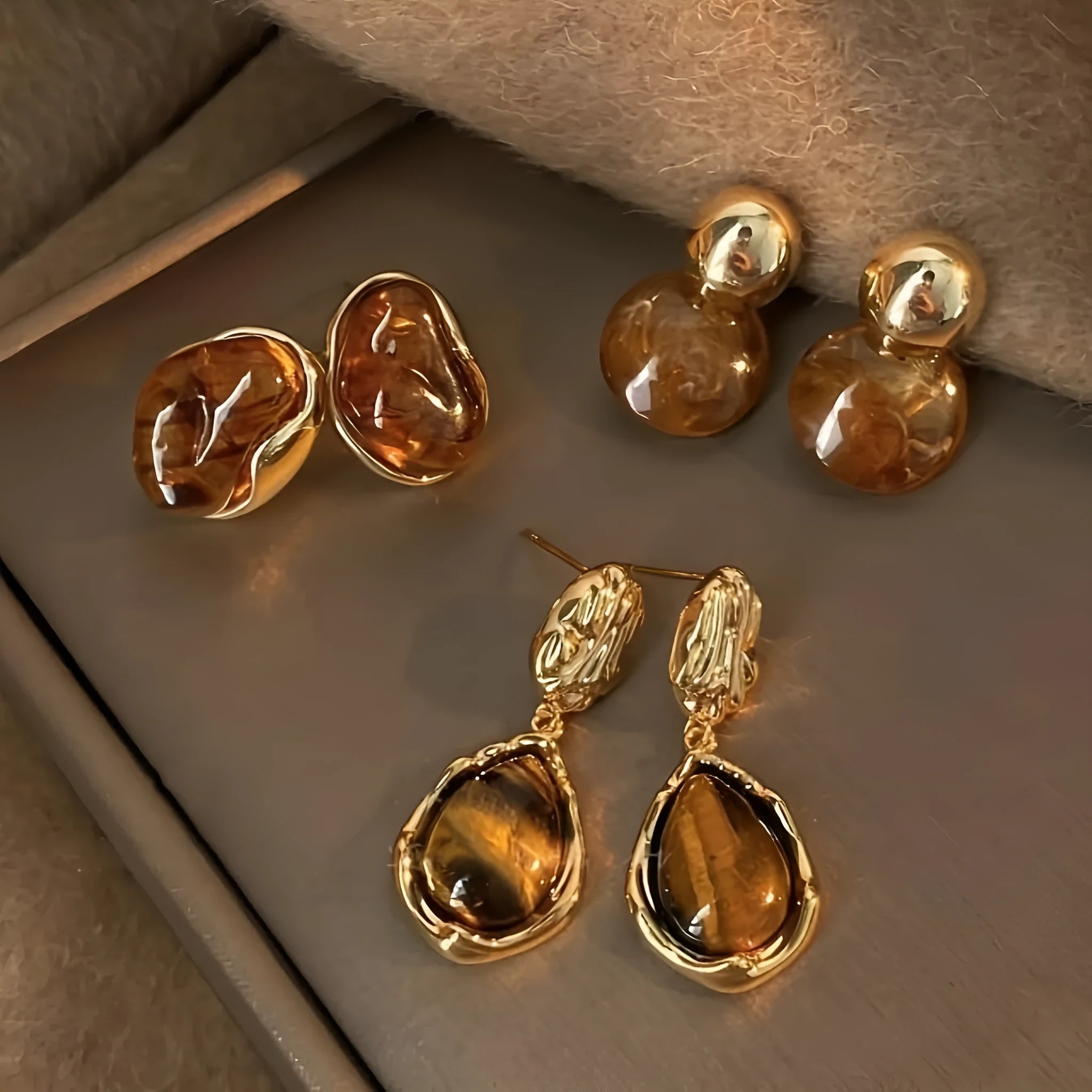 Set of three pairs of geometric holiday earrings: round studs, irregular amber studs, and tassel drop earrings.