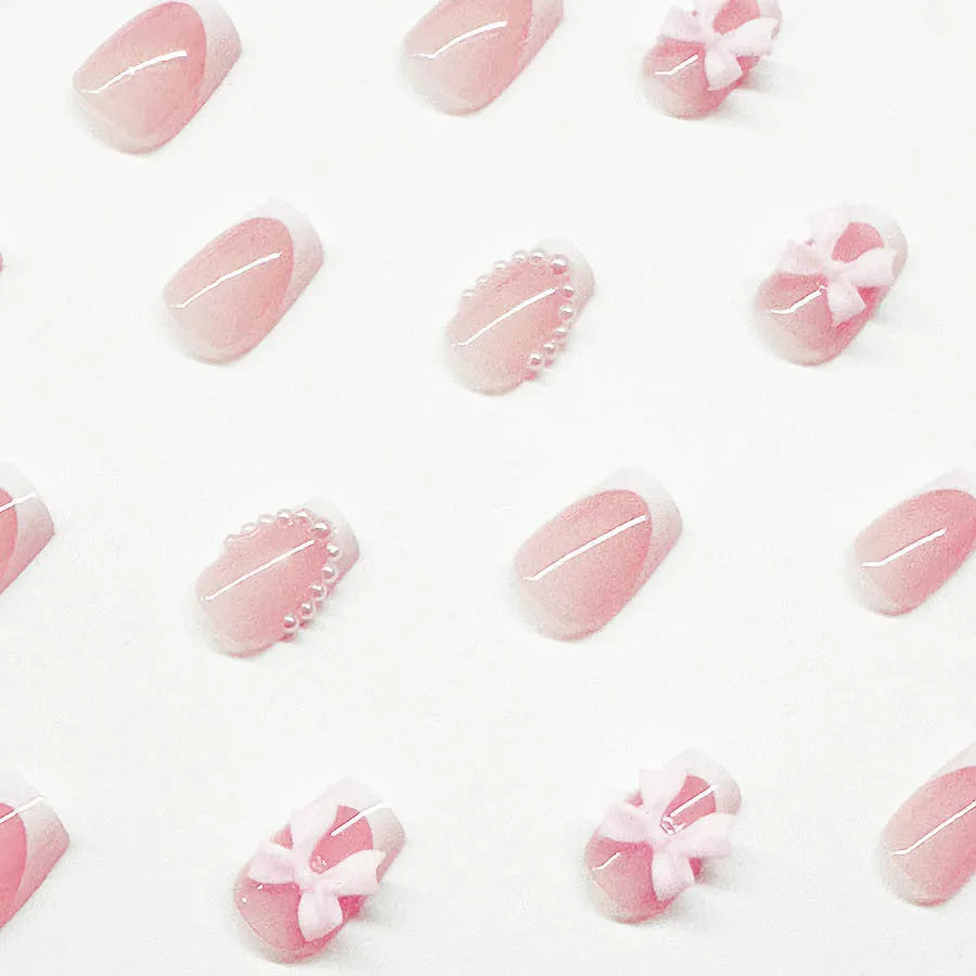 Short white French tip press-on nails with a cute pink bow design and a tulip pattern on a blush base.