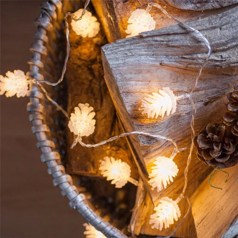 Warm white LED pine cone decorative light string powered by batteries on a green foliage background.