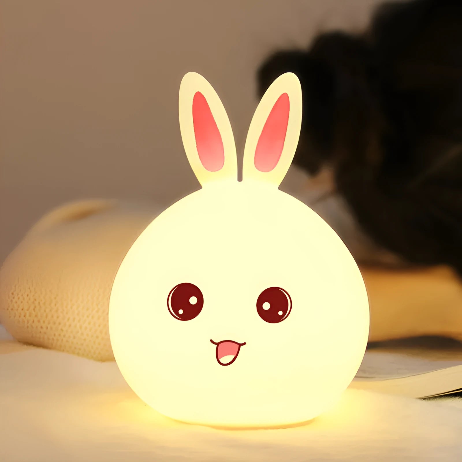 Cute rabbit-shaped night light made of soft silicone with touch sensor, showing seven LED colour options, on a bedside table.