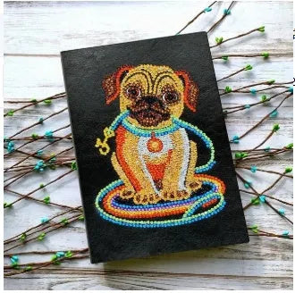 Black A5 hardcover diamond painting notebook with elastic closure, shown closed and open on a crafting table.