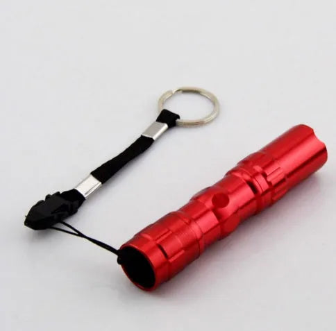 Black aluminium mini LED flashlight showing scale next to a AA battery.