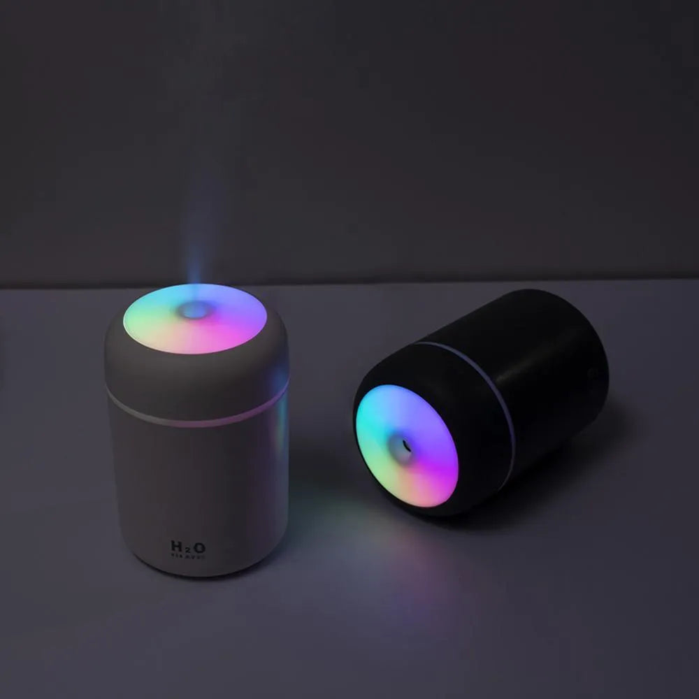 Pink USB desktop humidifier with coloured LED lights and water tank on a wooden desk.