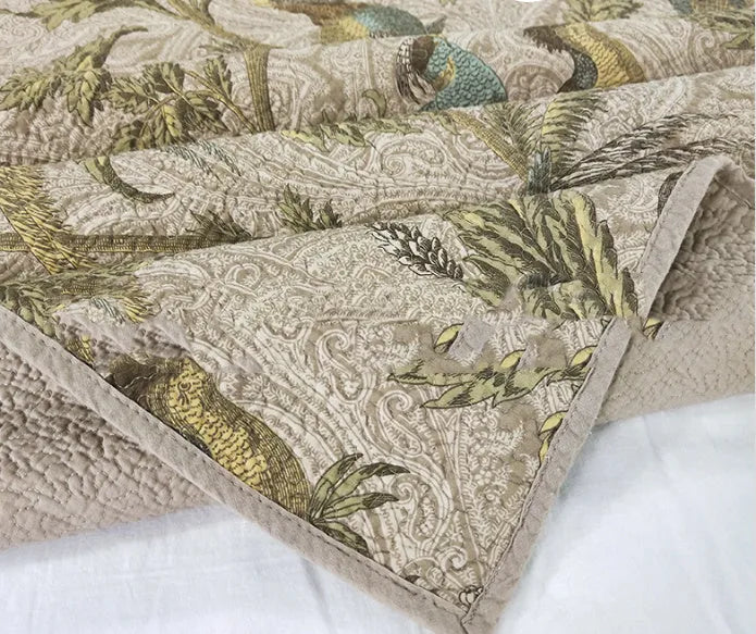 Blue American-style floral and bird quilted cotton bedspread set on a bed, showing textured stitching.