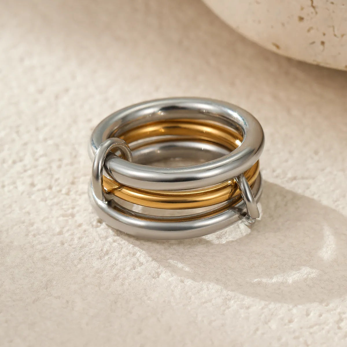 Stacked gold plated stainless steel rings with an exaggerated design on a person's hand.