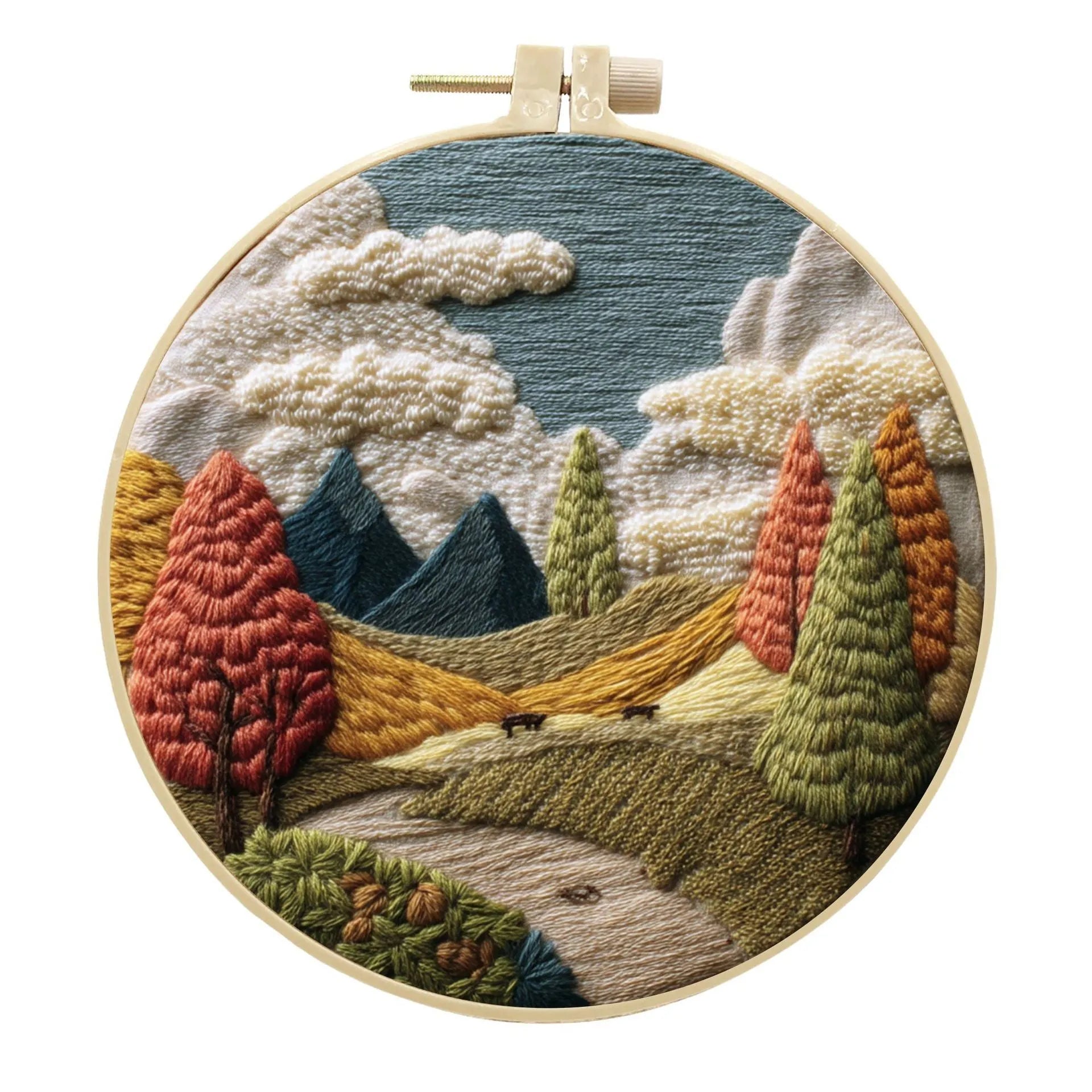 Embroidery DIY kit components: printed landscape fabric, embroidery hoop, coloured threads, and needles laid flat.