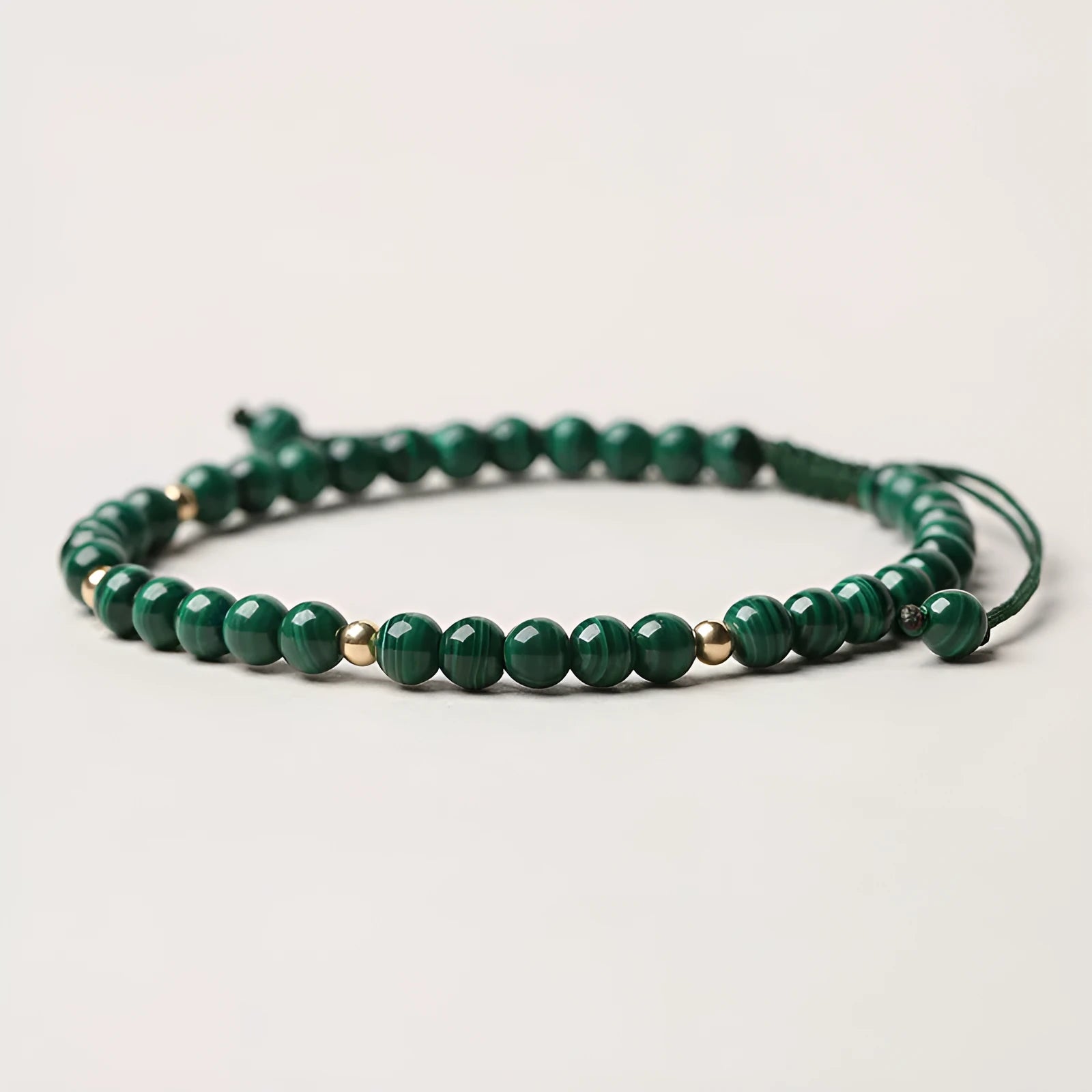 Natural green malachite crystal bracelet with golden balls on a woven hand strap.