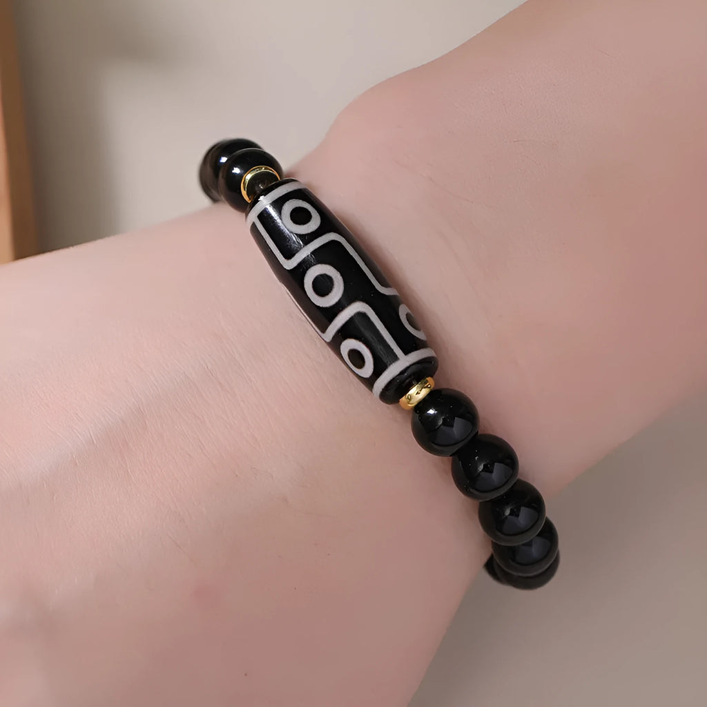 Close-up of a black obsidian dzi bead agate bracelet with adjustable cord, showing ethnic Tibetan design.