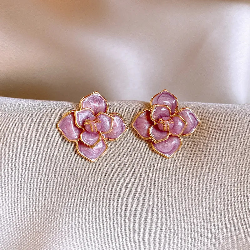 Close-up of gold plated purple flower stud earrings with iridescent oil-spot glaze on a copper base.