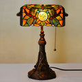 Colourful Tiffany-style stained glass table lamp with resin base on a wooden desk.