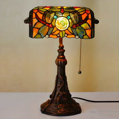 Colourful Tiffany-style stained glass table lamp with resin base on a wooden desk.