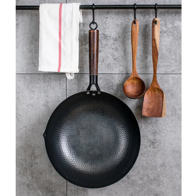 Traditional black cast iron wok with a long wooden handle, shown with a glass lid.