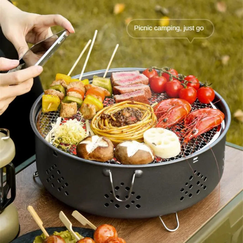 Portable stainless steel barbecue grill with detachable parts on a grassy outdoor surface.