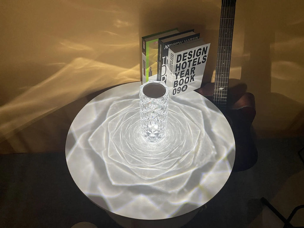 Clear acrylic crystal rose shaped LED table lamp with diamond-like facets on a table.