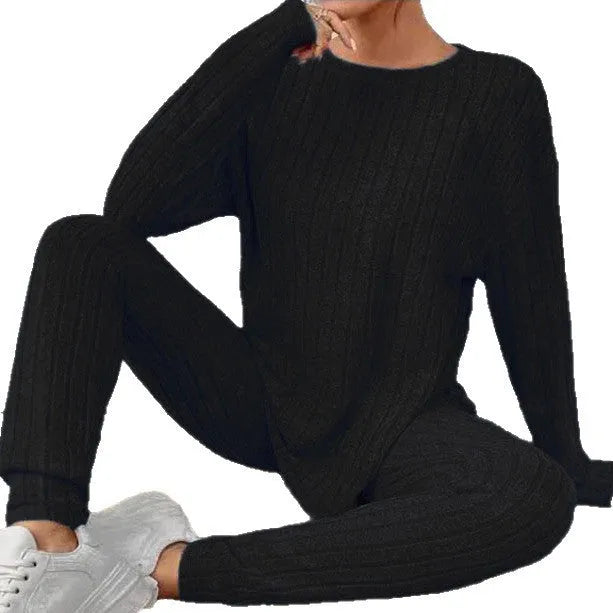 A woman wearing a black sunken stripe two-piece loungewear set, consisting of a regular-sleeve top and elasticated waist trousers.