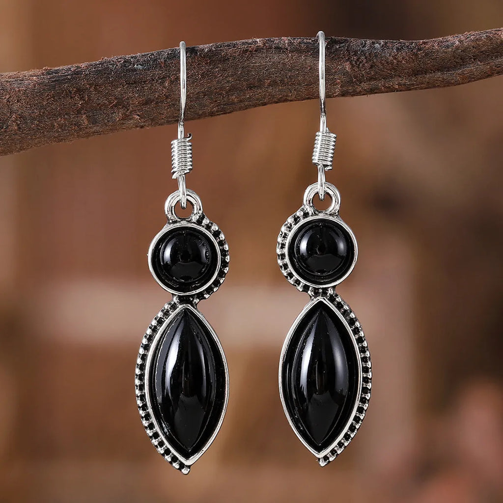 Close-up of vintage black and purple geometric drop earrings with a circular pendant on a long chain.