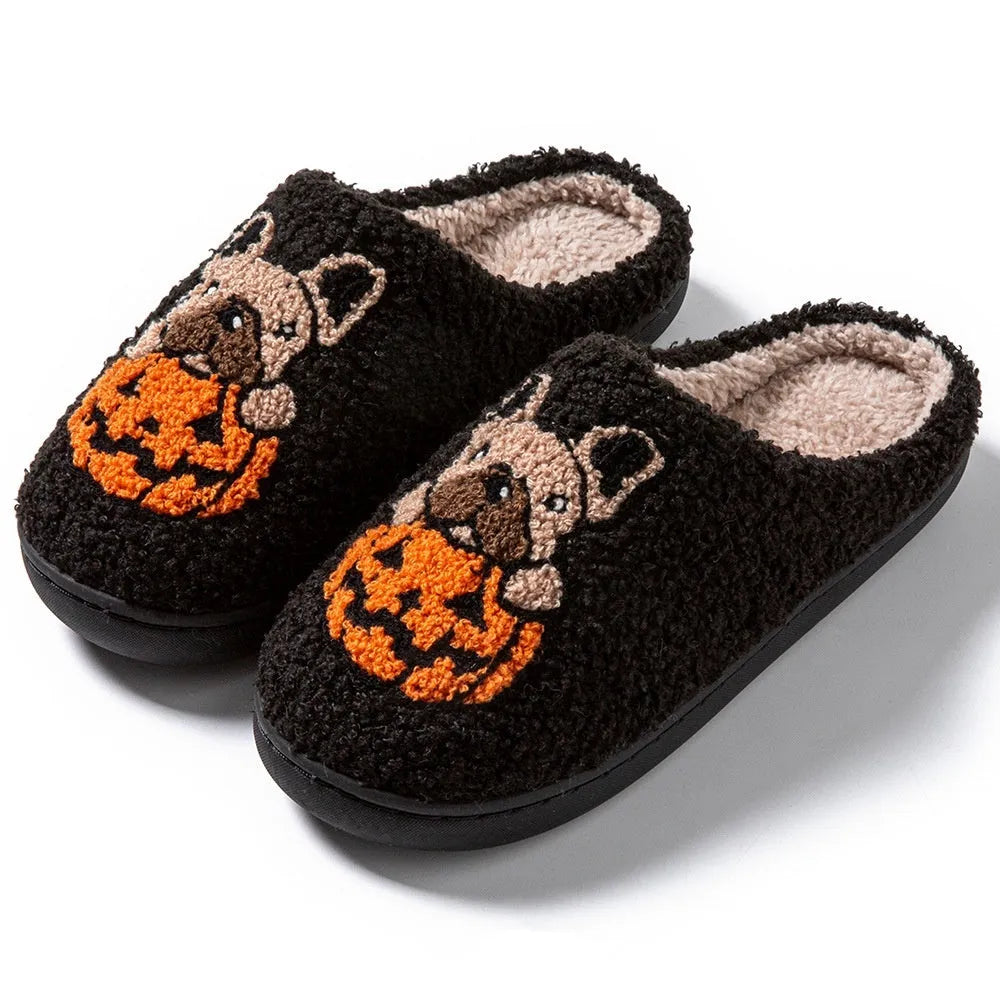 Black Halloween slippers with pumpkin print, plush fabric, and thick textured TPR rubber soles on a wooden floor.