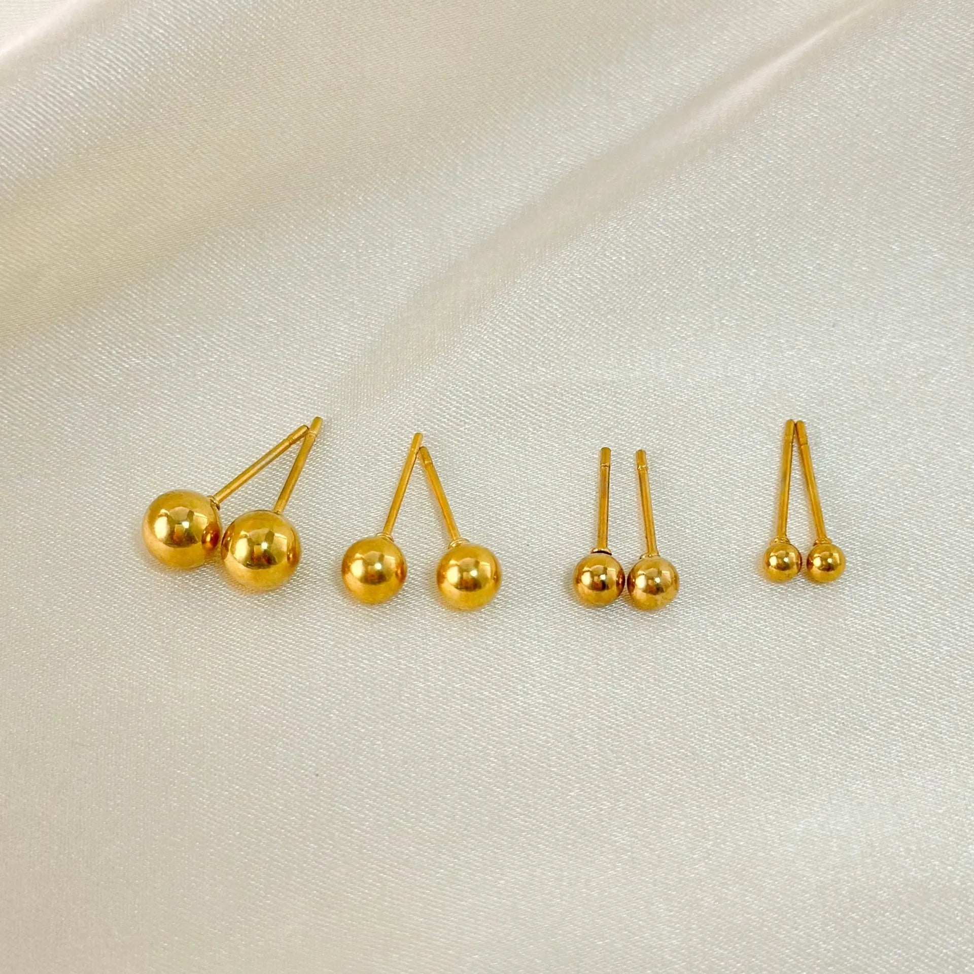 Simple gold-coloured stainless steel ball stud earrings in geometric design on a white background.