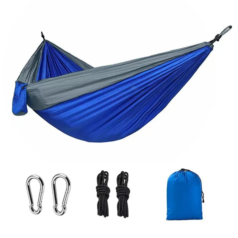 Blue parachute nylon camping hammock hung between two trees, showing its full 270cm length and attachment carabiners.