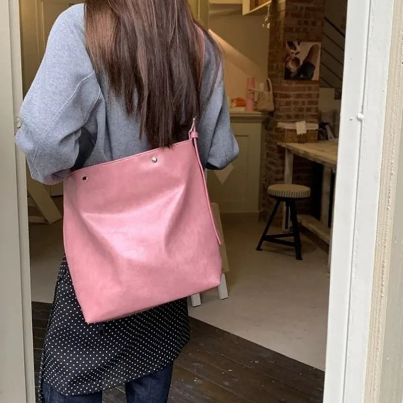 Corduroy one-shoulder messenger bag in pink on a table, showing adjustable strap and structured shape.