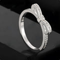 Silver coloured ring with a detailed bow shape set with clear sparkling zircon crystals on a model's hand.