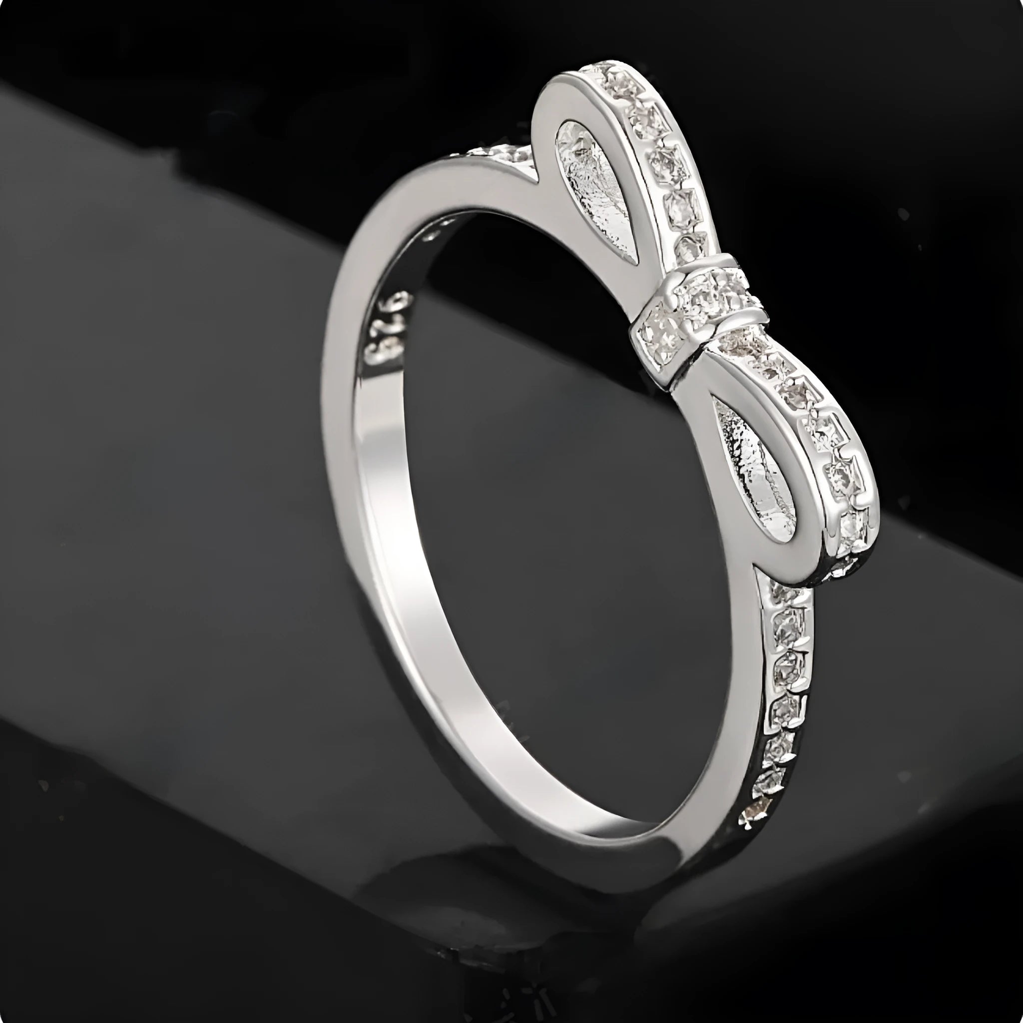Silver coloured ring with a detailed bow shape set with clear sparkling zircon crystals on a model's hand.