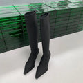 Women's black pointed toe knee-high boots with a stiletto heel and a back zip, shown on a foot.