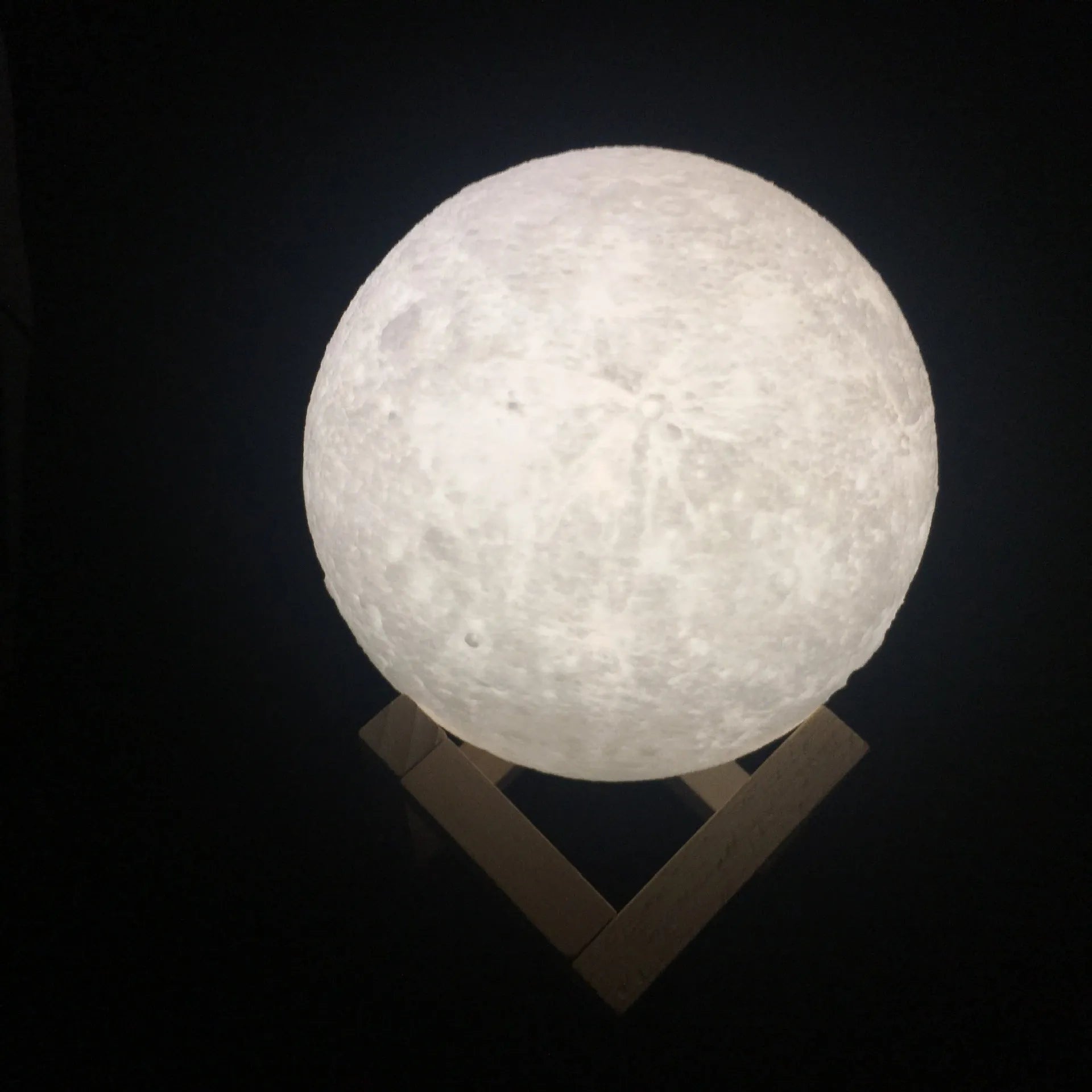 3D printed white moon lamp on a wooden holder, showing detailed lunar surface and a glowing yellow light.