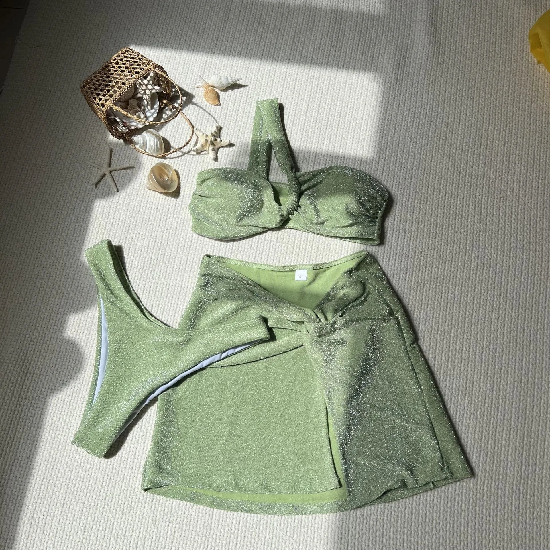 Light green one-shoulder glossy swimsuit three-piece set with matching skirt and pants.