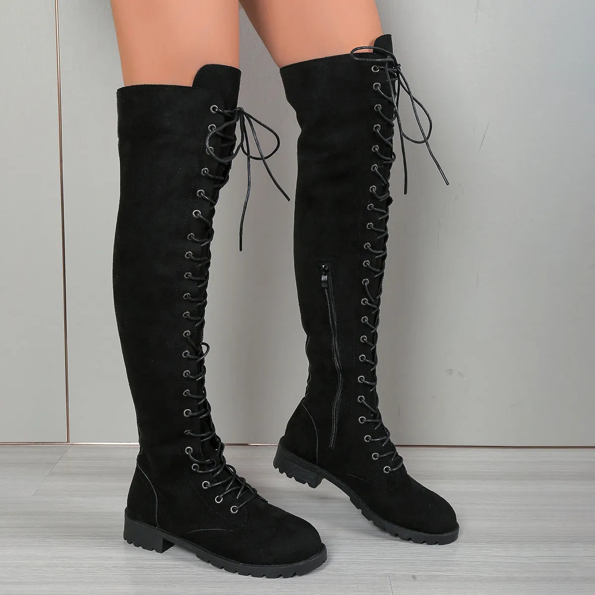 Black lace-up over-the-knee boots with a round toe and flat sole on a neutral background.