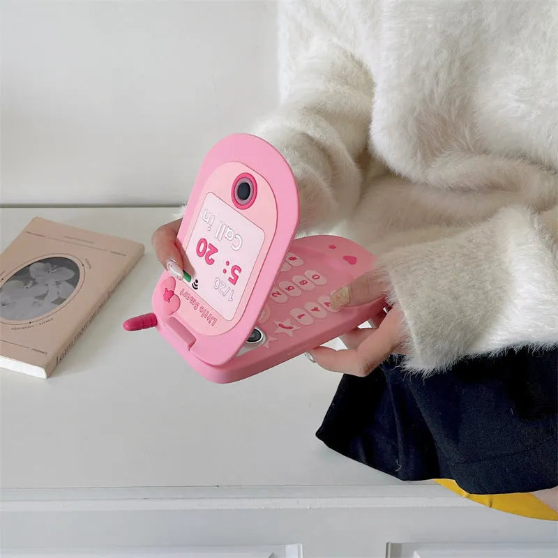 Light pink silicone flip phone case with a pop-out mirror and a cartoon charm, shown next to an iPhone.